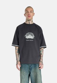 Black short-sleeve t-shirt with a graphic print at the center. Features white stripes on sleeves and a relaxed fit. Cotton material.