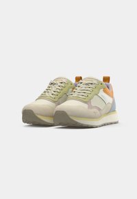 Une paire de baskets au style rétro avec des panneaux beige, vert, orange et bleu, des lacets blancs et des semelles épaisses de couleur crème sur un fond blanc.