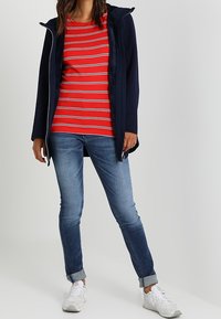 Laivastonsininen vetoketjullinen takki, jonka alla punavalkoraidallinen paita, yhdistetty vaaleansinisiin, käännetyillä lahkeilla varustettuihin farkkuihin ja valkoisiin tennareihin.