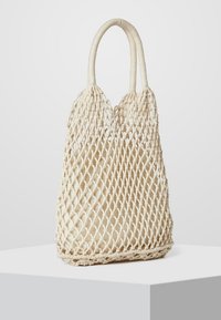 Woven natural fiber bag in cream, featuring a mesh design, two curved handles, and a spacious interior. Ideal for casual use.