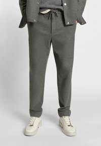 Grå, texturerade joggerbyxor med elastisk snörning i midjan och sidofickor, tillsammans med vita sneakers.