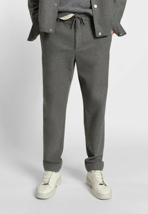 Grå, strukturerede joggingbukser med elastisk snor i taljen og sidelommer, parret med hvide sneakers.