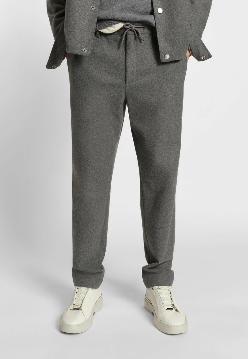 Grå, texturerade joggerbyxor med elastisk snörning i midjan och sidofickor, tillsammans med vita sneakers.