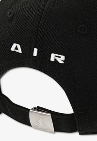 Μαύρο καπέλο από ύφασμα με λευκά κεντημένα γράμματα "AIR" στο πίσω μέρος. Το μεταλλικό κούμπωμα διαθέτει λογότυπο με σιλουέτα αθλητή που πηδάει.