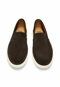 Brune semskede slip-on sko med hvite gummisåler, med sydd detaljer og en glatt tekstur. Merkevaren logo er synlig på innsiden.