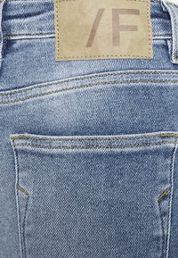 Modré džíny z denimu s hnědou koženou etiketou na pase, žlutým prošíváním a zadní kapsou s vyztuženým švem.