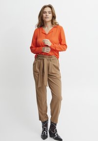 Orange långärmad skjorta med krage, kombinerad med högmidjade tan-byxor med ett bälte. Svarta klackboots med vita accenter.