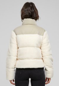 Doudoune avec une partie supérieure beige et un bas en polaire texturée crème. Dispose d'un col haut et d'un design court avec des manches larges.