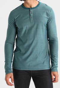 Türkisfarbene Langarm-Henley-Bluse aus strukturiertem Stoff, mit Rundhalsausschnitt und kontrastierenden Besätzen sowie einer dreiknöpfigen Knopfleiste.