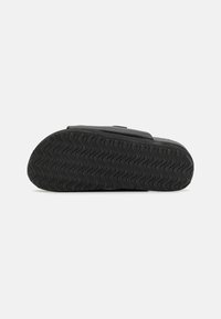 Black rubber sandal sole featuring a wavy texture, flat design, and an open toe. The upper part is not visible in the image.