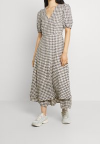 Rutig klänning i beige och marinblå med V-urringning, puffärmar och en lager-på-lager fåll; kombinerad med ljusa sneakers. Lättviktig tyg.