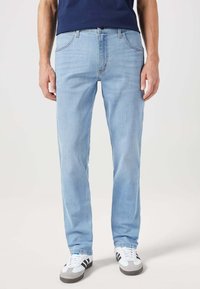 Jeans azzurri chiari con un design a gamba dritta, stile classico a cinque tasche e dettagli di cucitura sottili, abbinati a sneakers bianche.