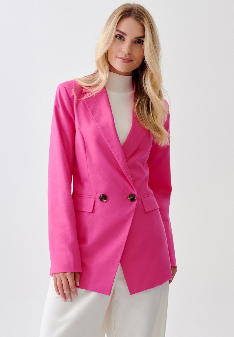 Blazer de doble botonadura en rosa fuerte con solapas muestradas, dos bolsillos frontales y botones marrones. Tejido suave con un corte entallado.