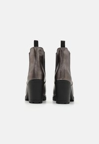Botines de cuero gris con una textura suave, tacones altos de bloque, tiradores y costuras verticales a los lados. Puntas redondeadas.