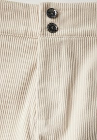 Beige kordfrott�étyg med vertikala ribbor, med två svarta knappar vid midjan och en sidoficka.