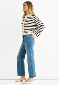 Crocheted cardigan in cream with black stripes, button front, relaxed fit. Paired with light blue straight-leg jeans and two-tone pointed heels.