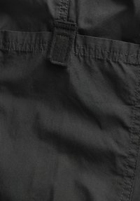 Tessuto nero con una texture liscia, caratterizzato da una toppa cucita e cuciture lungo i bordi. Include un piccolo anello per il fissaggio.