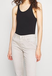 Svart ribbad tanktopp i kombination med ljusbeige slim fit-jeans, med en jämn yta, hög halsringning och standardfickor.