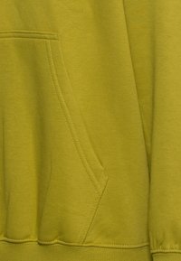 Tessuto di felpa verde dalla texture morbida, con tasca a marsupio e polsini a coste, mostrato in primo piano per evidenziare i dettagli.