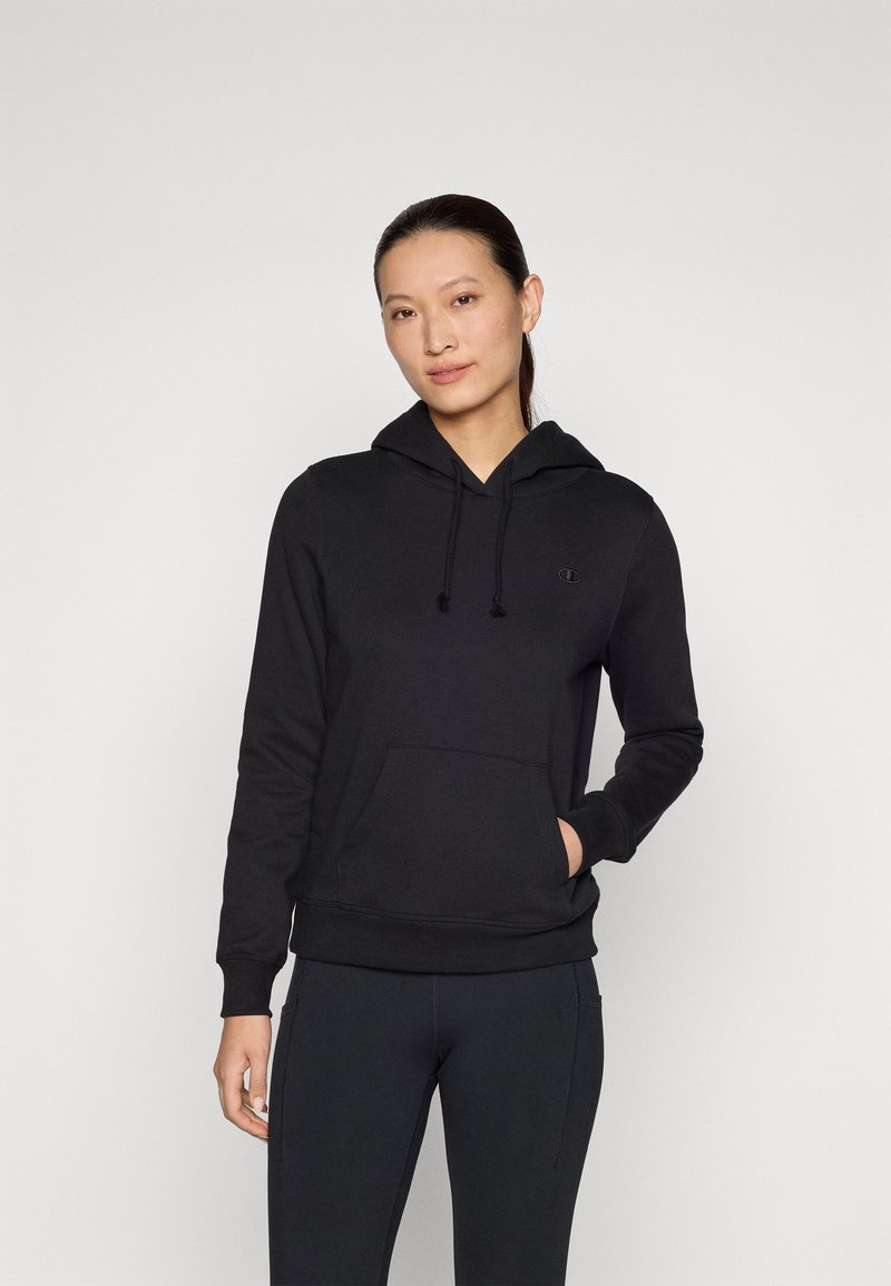 Svart hoodie i mjukt material med känguruficka, dragsko i huvan och en subtil logotyp på bröstet. Stilen har en figurnära silhuett.