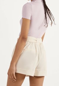 Světlofialový krátký top s jemným žebrováním, doplněný o krémové kraťasy s vysokým pasem, bočními kapsami a podhrnutými lemy.
