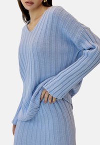 Pull en tricot bleu clair avec des rayures verticales, un décolleté en V et des manches longues, présentant une coupe décontractée et un tissu texturé.