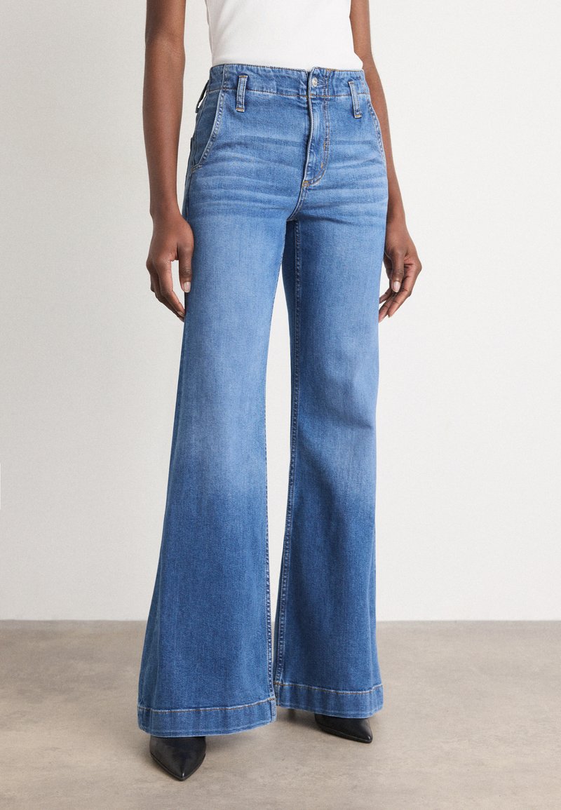 Jean en denim bleu à taille haute et jambe large, avec un léger délavage et des coutures contrastées, complété par un design classique à cinq poches.