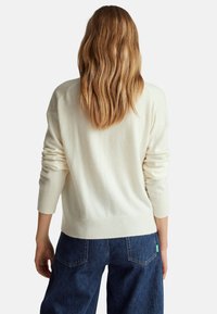 Krémový svetr s žebrovanými manžetami a lemem. Měkká textura, uvolněný střih. Nosit s tmavě modrými džíny s vysokým pasem a náprsními kapsami.