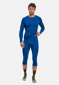 Blue long-sleeve top and matching capri leggings made of stretch fabric. Features ribbed texture and logo detail. Worn with striped socks.