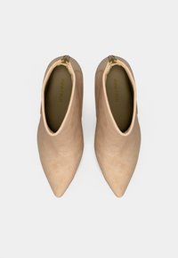 Ghete bej până la gleznă, cu vârful ascuțit, realizate din piele întoarsă netedă. Dispun de un fermoar lateral și un design minimalist. Interiorul afișează logo-ul brandului.