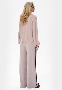 Lichtroze blouse met lange mouwen gecombineerd met grijze broek met wijdere pijpen en een donkere zijkantstreep. Soepele stof met een relaxte pasvorm.