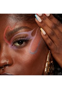 Primo piano di un occhio con trucco multicolore in forme rosse, viola e blu. Pelle lucida di colore marrone, ciglia bold e orecchino a cerchio dorato.