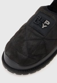 Czarne wsuwane buty z pikowanej zamszowej cholewki, gumową podeszwą i wyraźną czarną łatką z logo po boku.