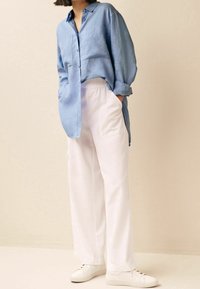 Chemise en lin bleu clair à manches longues avec col boutonné, associée à un pantalon blanc à jambes larges et des baskets blanches.