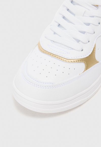 Vita sneaker med slät läderöverkänsla, guldfärgad detalj på sidan, rund tå och perforeringar för ventilation. Platta vita snören och sula.