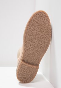Zapato de ante beige con una suela de goma texturizada en color beige. La suela presenta una superficie con un patrón para ofrecer agarre y es ligeramente redondeada en la punta.