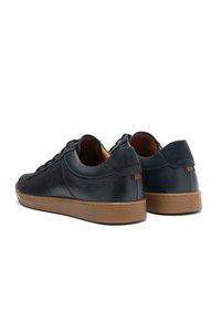 Črne usnjene superge z teksturiranim zaključkom, rjave gumijaste podplate, zaobljena oblika, minimalistična zasnova in diskretne šivalne podrobnosti.