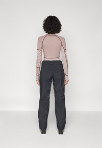 Long-sleeve, fitted top with a geometric pattern in light pink and dark red. Paired with loose black pants made of a waterproof material.
