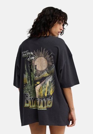 Maglietta nera oversize con una grafica colorata del deserto sulla schiena, che include un sole, cactus e la scritta "Billabong" in carattere grassetto.