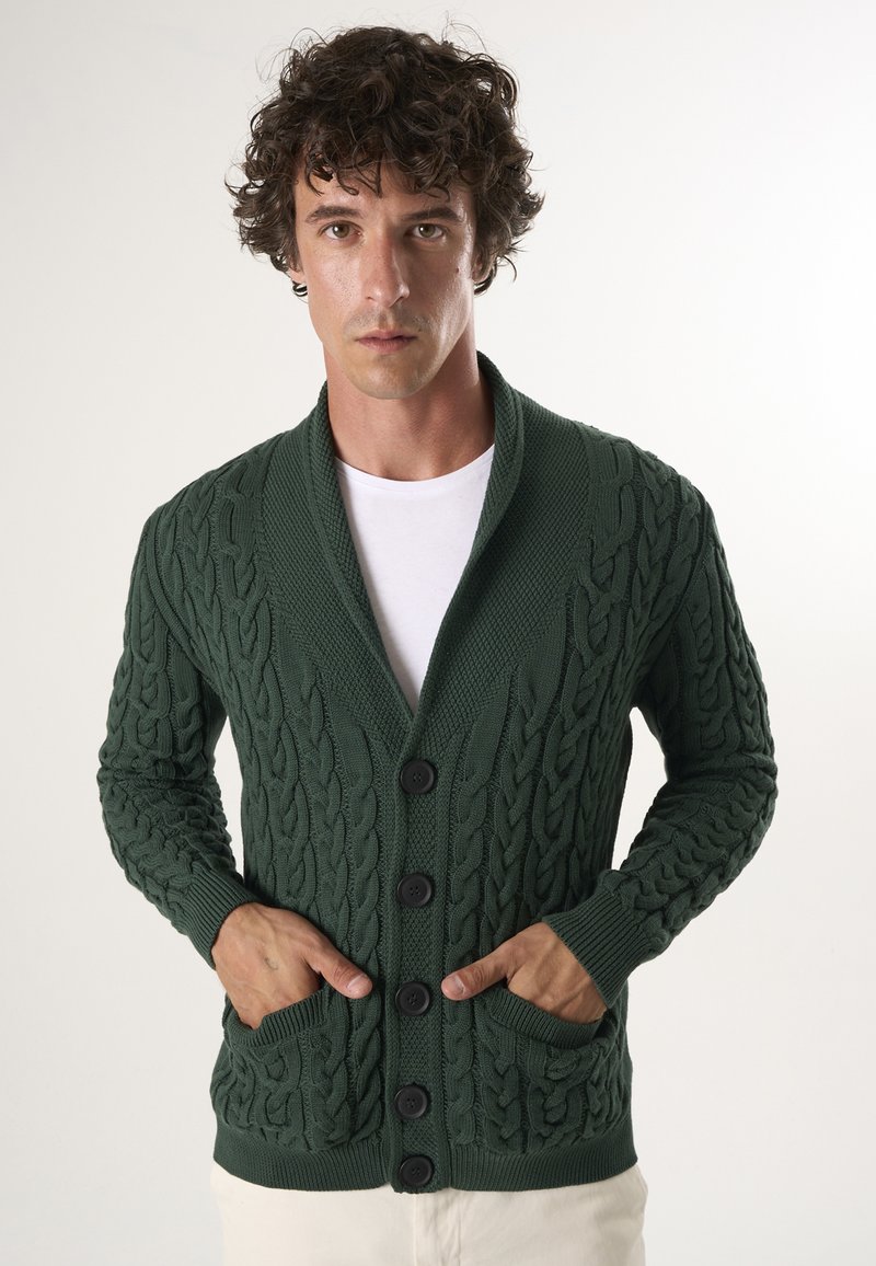 Grøn strikket cardigan med sjalkrave, prydet med teksturerede kabelmønstre, to forlommer og sorte knapper.