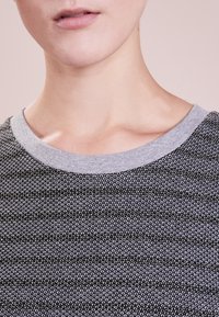Černý a šedý pruhovaný svetr s jemnou texturou, obsahující šedý kulatý výstřih a jemné metalické vlákna propletená v látce.