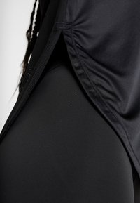 Svart atletisk topp med sidofåll och nätavslut, tillsammans med enfärgade svarta leggings i en mjuk, elastisk tyg.