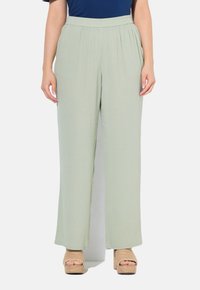 Lichtgroene, wijde broek met een geplaatste tailleband, met een gladde textuur. Gepaard met beige plateau-sandalen.