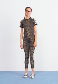 Set di abbigliamento sportivo con stampa leopardata nei toni del marrone e nero. Top a maniche corte con dettagli neri e leggings coordinati, abbinati a scarpe bianche e nere.