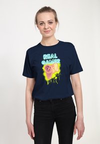 Navy blue cotton t-shirt featuring a neon graphic design of a game controller with "REAL GAMER" text and colorful paint splatter accents.