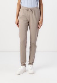 Beiga joggers i mjukt tyg, med elastisk midja och snörning, smalnande ben och ribbade avslut vid vristerna, kombinerat med vita sneakers.