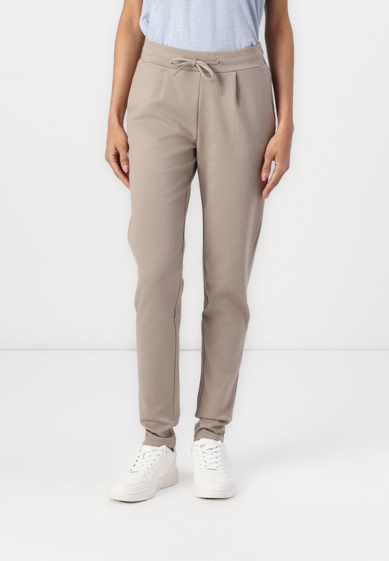 Beiga joggers i mjukt tyg, med elastisk midja och snörning, smalnande ben och ribbade avslut vid vristerna, kombinerat med vita sneakers.