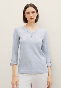 Camisa henley de manga larga en azul claro, hecha de un material texturizado. Presenta tres botones a lo largo del escote y puños enrollados.