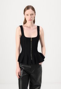 Μαύρο πλεκτό τοπ με τετράγωνη λαιμόκοψη, διαθέτοντας κεντρικό φερμουάρ και φουσκωτό τελείωμα. Η ραφημένη υφή προσθέτει λεπτομέρεια. Συνδυασμένο με μαύρο δερμάτινο παντελόνι.