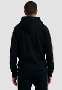 Sudadera negra con capucha, bolsillo tipo canguro en la parte delantera, capucha con cordón y franjas laterales en rojo y blanco que contrastan. Tejido suave y texturizado.